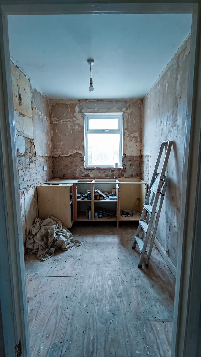 A kitchen mid renovation, bare walls and a plywood subfloor